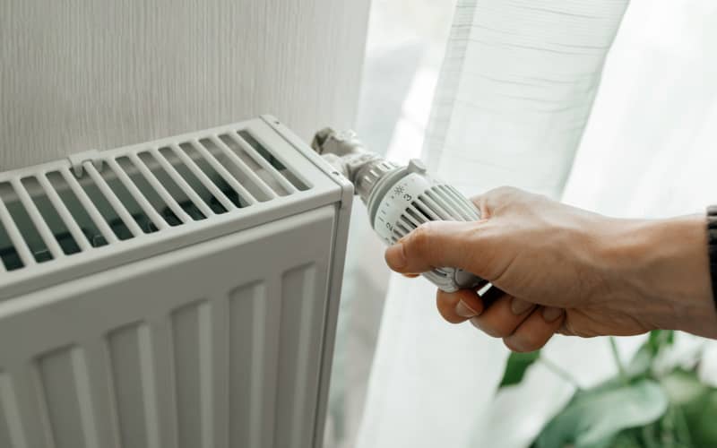 Mano ajustando la válvula de un radiador, acción relacionada con el proceso de purgar los radiadores.