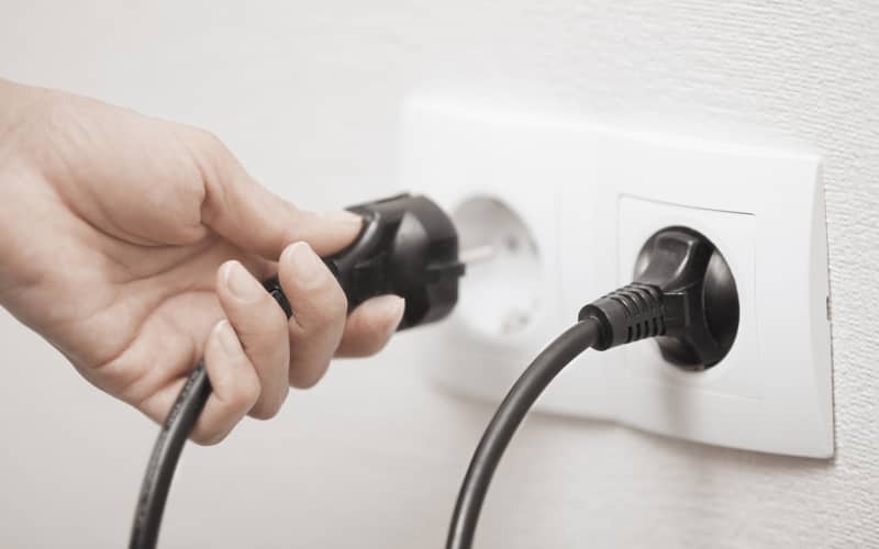 Una mano cogiendo un cable para conectarlo al enchufe