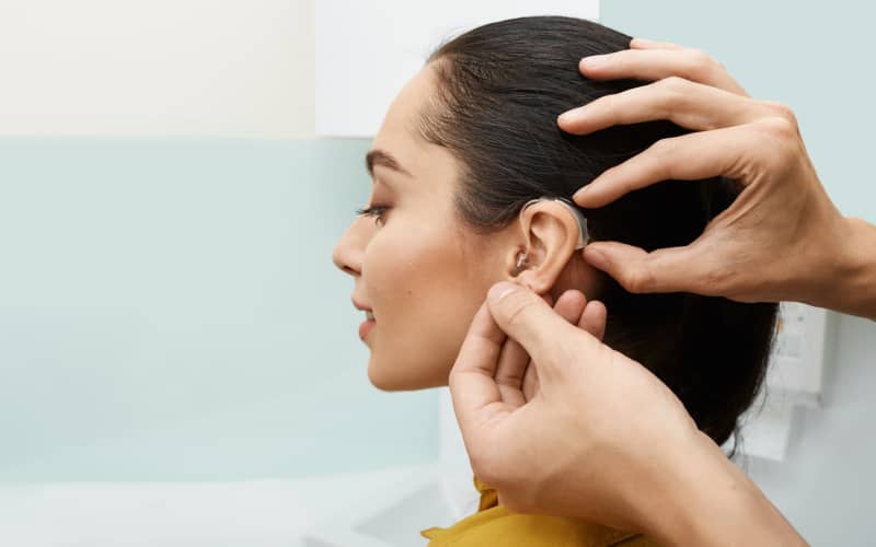 discapacidad-por-perdida-auditiva-01 Mujer con el pelo retirado de la cara mostrando el sonotone en su oído para tratar su discapacidad por pérdida auditiva.