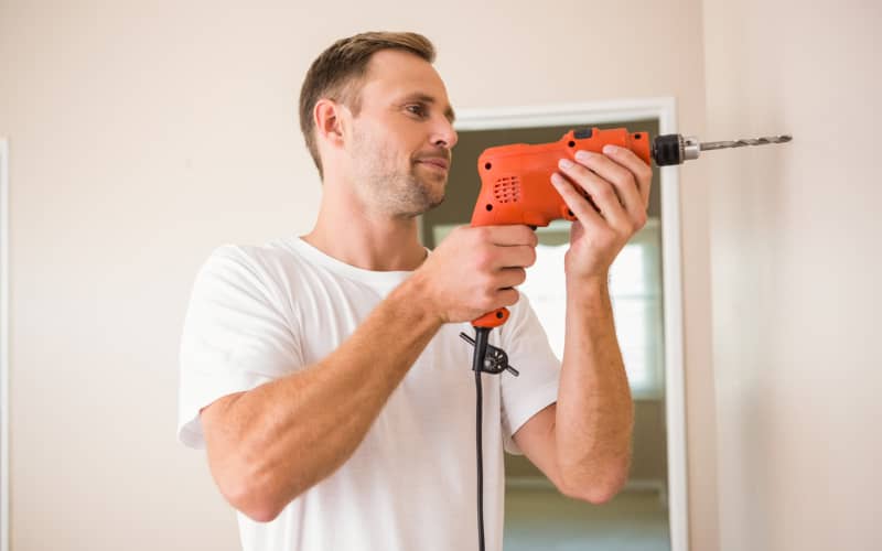 Hombre con un taladro en la mano cerca de una pared de una casa ejemplificando cómo usar un taladro