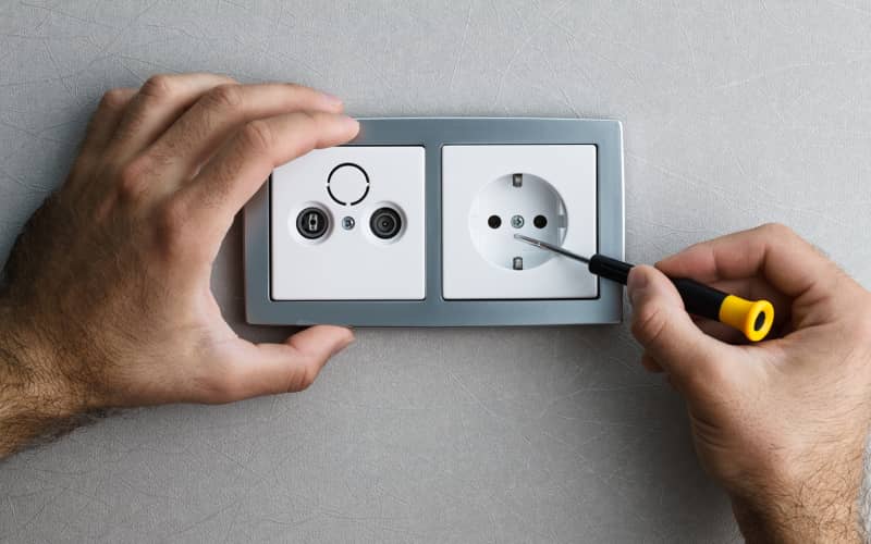 Manos manipulando una caja de conexiones y ajustando un tornillo de un enchufe con un destornillador, ilustrando el proceso de instalar un enchufe con interruptor de forma segura