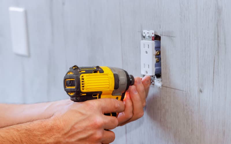 Manos utilizando un taladro para fijar un enchufe en la pared durante el proceso de instalar un enchufe con interruptor de forma segura