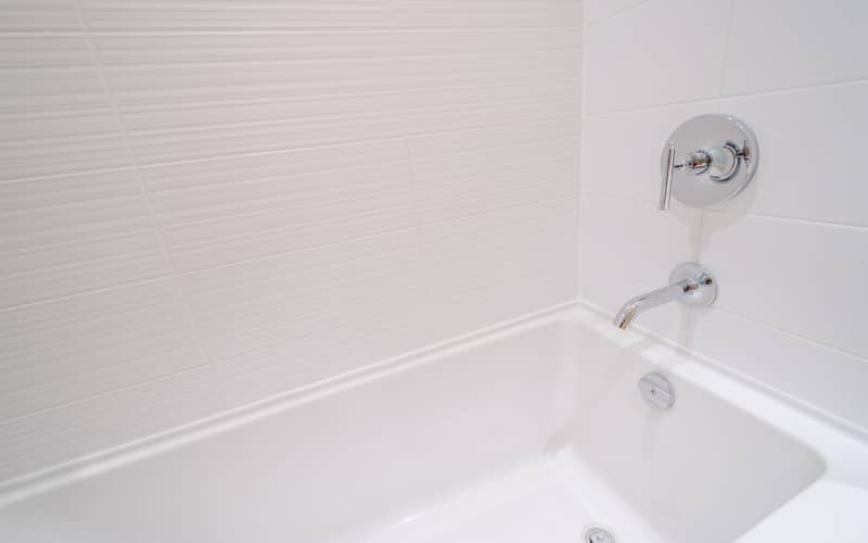 Bañera blanca con juntas de silicona en buen estado junto a una pared de azulejos y grifería cromada en un baño limpio.