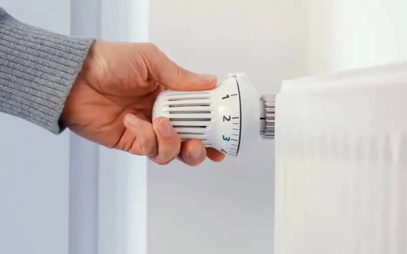 Mano girando la válvula termostática de un radiador, paso previo habitual en el proceso de cómo purgar los radiadores.