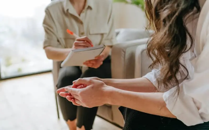 Mujer en sesión de terapia psicológica con una profesional de la salud mental, ambas sentadas y conversando en un entorno cómodo. La imagen representa el apoyo profesional en casos de discapacidad invisible.