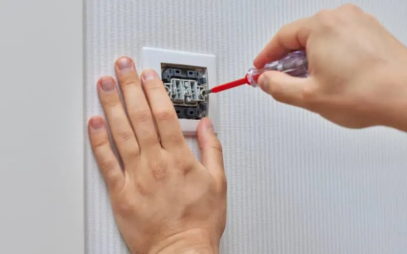 Manos manipulando un enchufe de la pared con un destornillador, en representación del proceso de instalar un enchufe con interruptor 