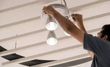 Hombre instalando una lámpara de techo con tres focos en un techo moderno con listones, ejemplo práctico de cómo poner una lámpara de techo.