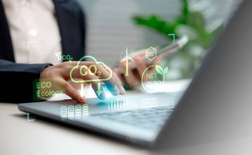 Manos de una persona escribiendo en su ordenador portátil con un diseño gráfico de emisiones sobreimpresos, en representación de la huella de carbono personal.